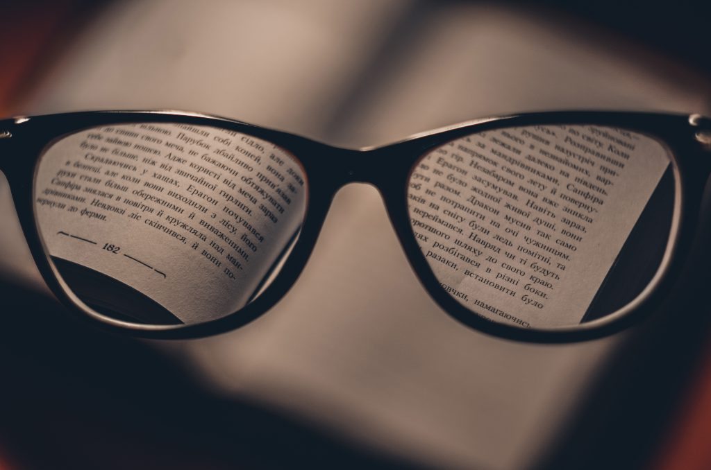 A pair of  black rimmed glasses held in front of a book, bringing the words into focus.