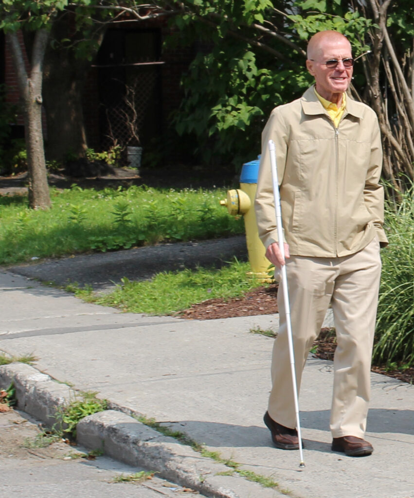 A man walking down a street with a white cane.